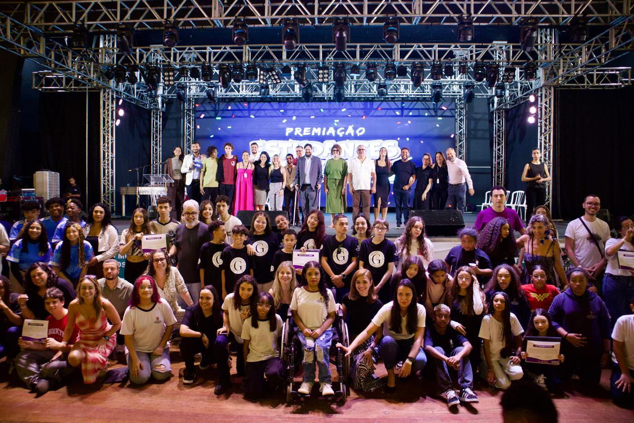 Foto dos representantes dos grêmios a frente do palco e organizadores no palco.