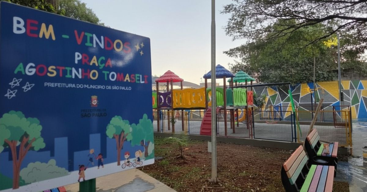 esquerda da imagem, em primeiro plano, há uma grande placa azul de boas-vindas. Em letras grandes e coloridas, ela diz: 