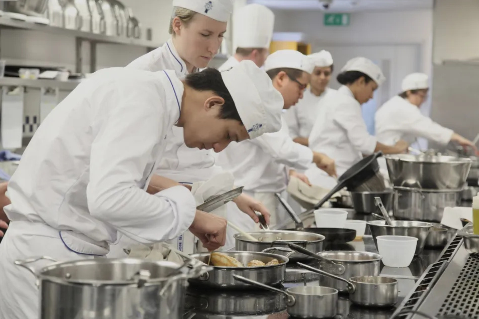 Alunos de culinária com aventais brancos cozinhando